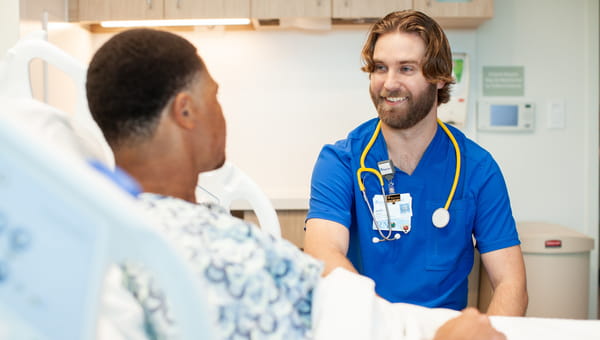 Male BayCare team member smiling at a patient in a hospital room.