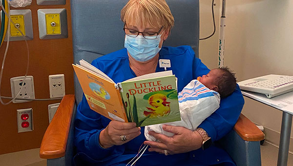 a woman wearing scrubs and a facemask reading a book to an infant