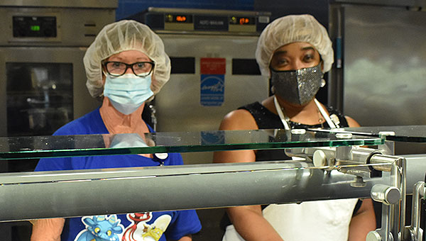 two woman wearing masks and hairnets in the cafeteria