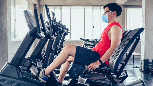 Young male on an exercise bike wearing a mask