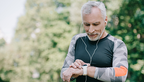 an elderly man outside wearing headphones looking at his fitbit
