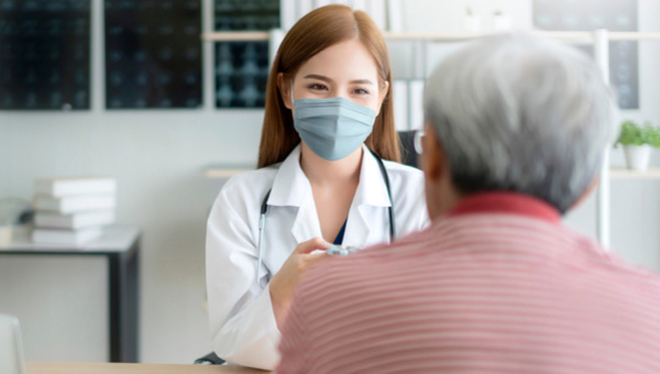A senior male patient is at an office visit with his female doctor, who is wearing a mask.