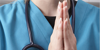 A woman prays wearing hospital scrubs and a stethoscope around her neck