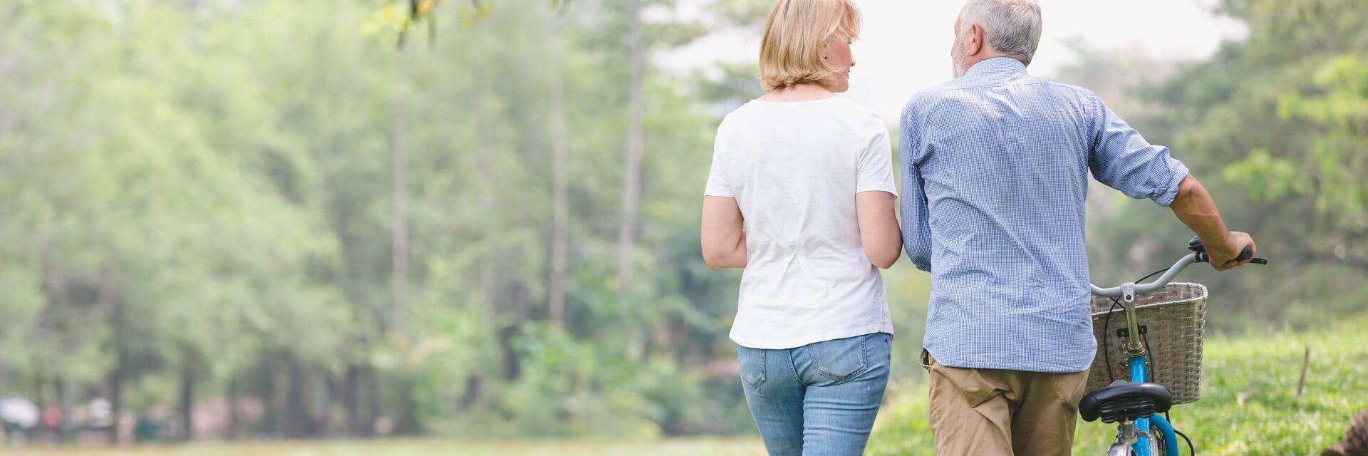 A couple is walking outdoors while the man pushes a bicycle.