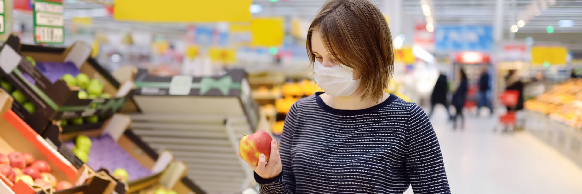 Lady in grocery store wearing a mask looking at an apple