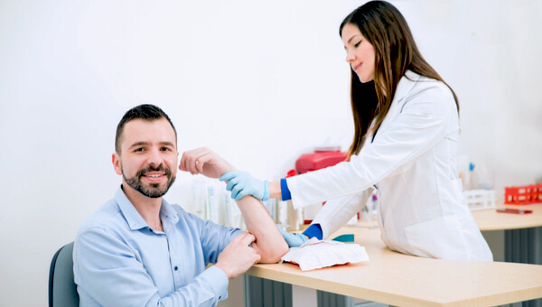 Un asistente de laboratorio posiciona el brazo de un hombre para una prueba de sangre