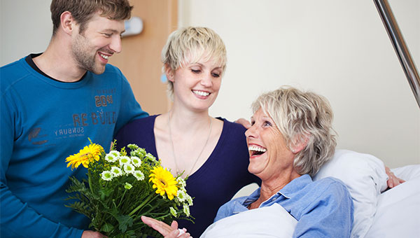 A smiling female patient receiving flowers from a male visitor and female visitor