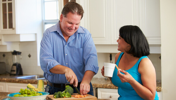 a man and woman smiling at each other in the kitchen preparing food