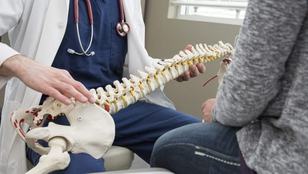 Spine Services A doctor holding a 3D model of a spine and discussing with a patient.