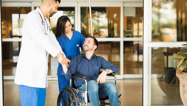 Happy and recovered patient sitting on a wheelchair and saying goodbye to his doctor while leaving the hospital