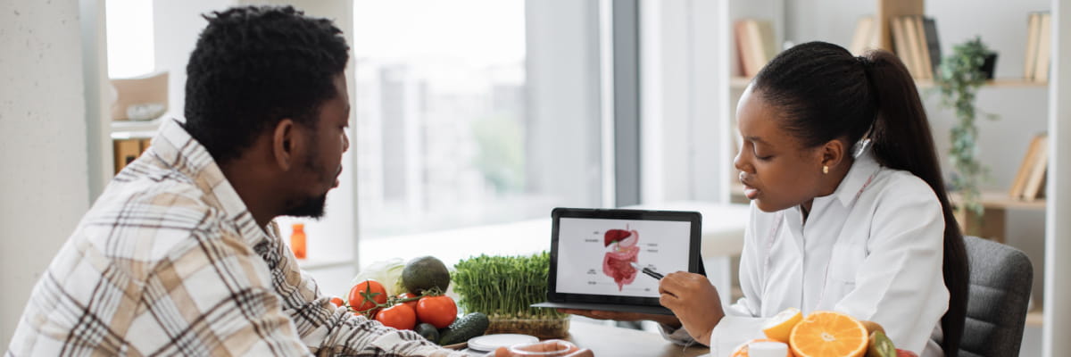 A female nutritionist sharing information about digestion on a tablet to a male patient in a well lit room.