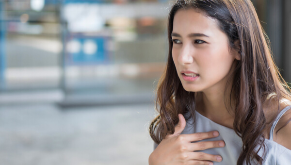 A young woman grimaces while holding her hand over her heart