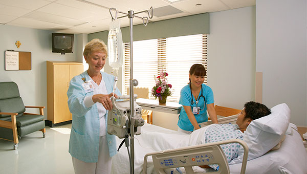 Two female nurses checking on a male patient in his hospital room