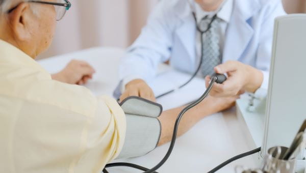 a physician wearing a labcoat taking the blood pressure of an elderly man