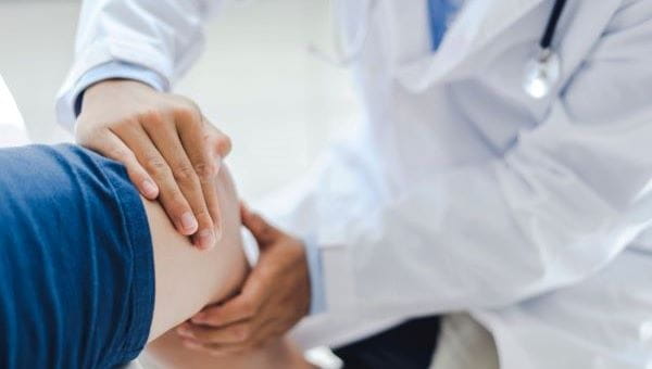 a physician wearing a lab coat placing both hands on a patients knee