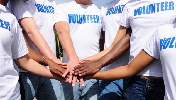 a group of people wearing white volunteer shirts putting their hands together