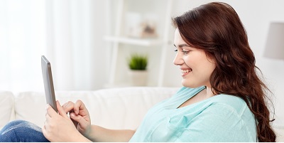 smiling young woman sitting on couch with tablet at home