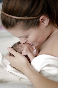 Mother holding newborn and kissing her on the head