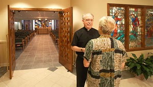 A priest speaking with a woman near the entrance of the chapel at St. Anthony's Hospital in St. Petersburg