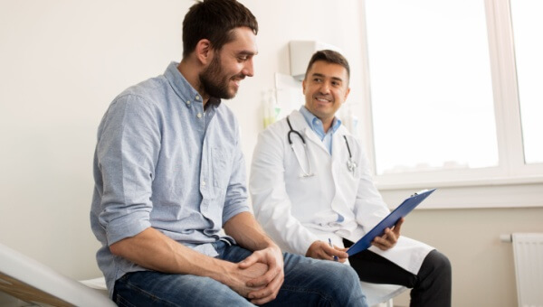 A male doctor sits with a male patient, looking at his patient chart. 