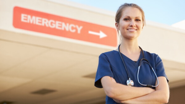 A female nurse stands in front of an Emergency sign. 