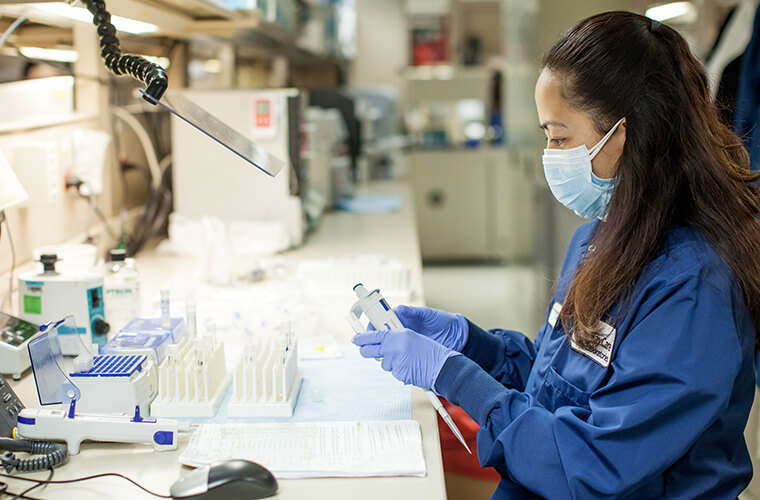 A female works in a medical lab wearing a mask and gloves