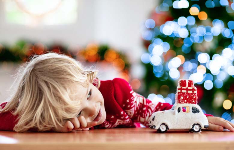 A child playing with a toy care with a Christmas tree in the background