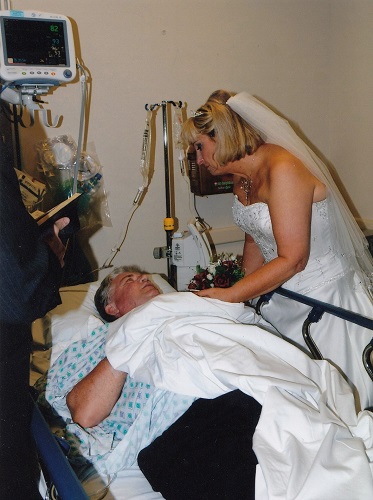 Dianna stands over Les in his hospital bed and comforts him