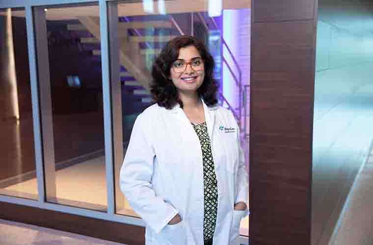 Dr. Stephanie Mattathil stands for a professional portrait while wearing her white coat.
