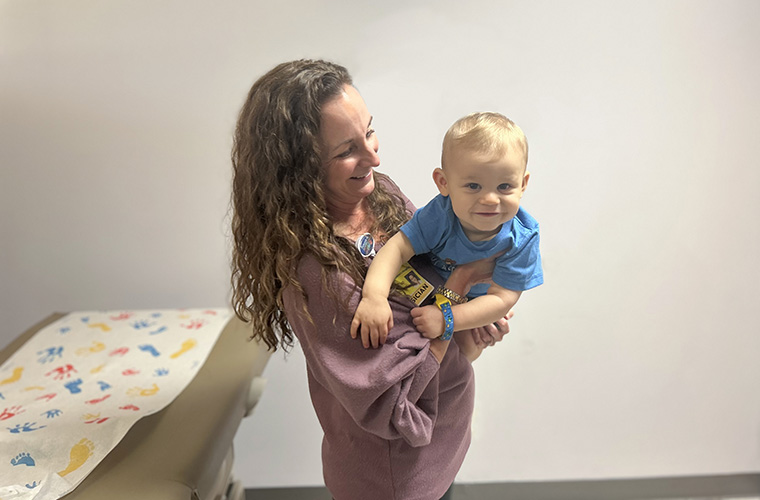 Physician who is Dr. Erin Cockrell at St. Joseph’s Children’s Hospital and has long brown hair and is wearing a pink top, is holding a baby who is her patient. The baby has blue eyes and blonde hair and is smiling. They are in a patient room. 