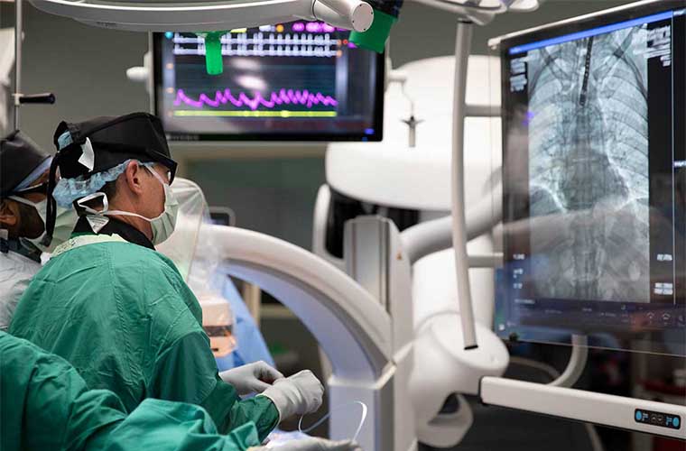 Two surgeons in scrubs looking intently at a monitor with a real-time picture inside of the patient’s chest.