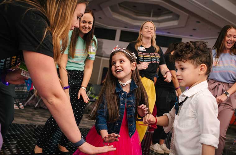 Young girl and boy dressed in party attire are having fun on the dance floor during St. Joseph's Children's Hospital prom. Hospital staff are dancing with the children and all are smiling and having fun.