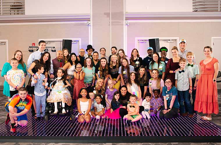 A group of pediatric patients of all ages and their families pose on dance floor with staff from St. Joseph's Children's Hospital during prom night at the hospital.