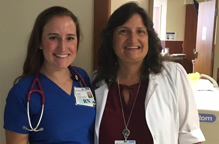 Two brunette, female nurses with a family resemblance stand together smiling in a hospital hallway.