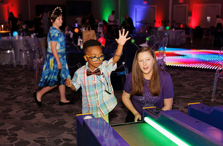 A young boy wearing a bow tie and a woman in a purple shirt play ski ball.