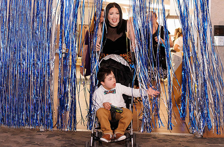 A woman pushing a young boy in a stroller enters a room through a tinsel curtain. 