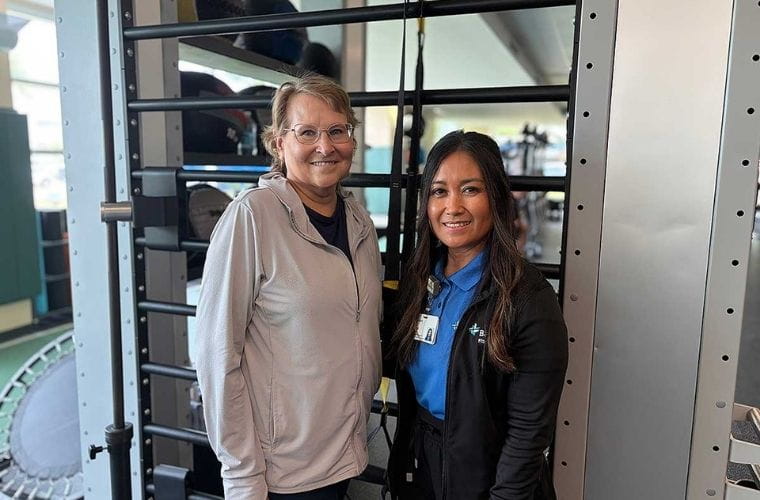 Two women standing in front of gym equipment, one wearing athletic clothing and the other in a BayCare uniform.