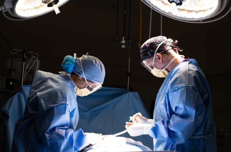 Two BayCare surgeons in blue scrubs perform a procedure in an operating room.