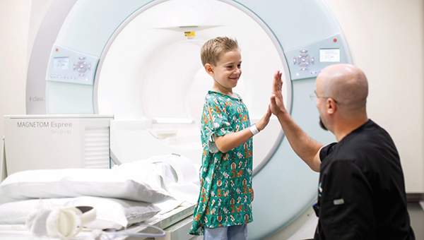 a boy in a hospital gown high fiving a technician