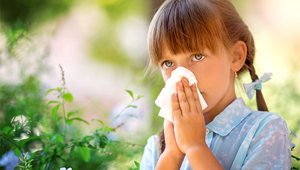 A little girl is blowing her nose into a tissue.