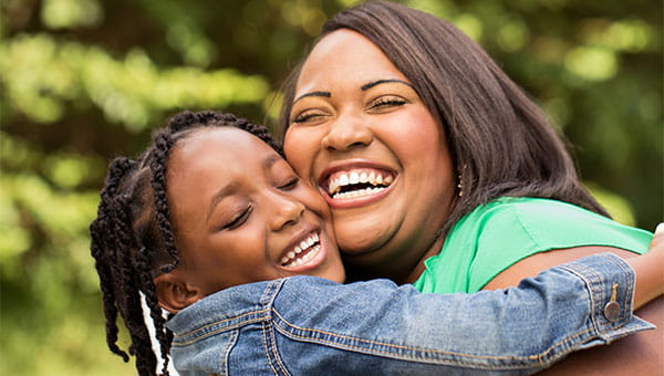 A smiling girl hugs her smiling mother.