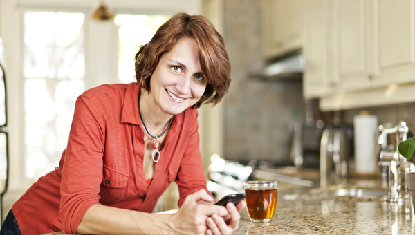 Smiling mature woman using mobile phone in kitchen at home