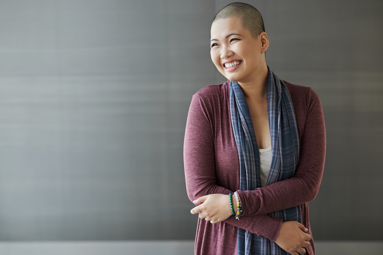 woman with shaved head smiling against gray background