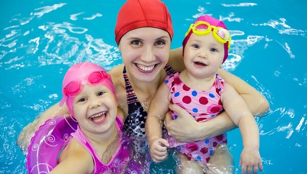 A mom is swimming in a pool with her two young daughters.