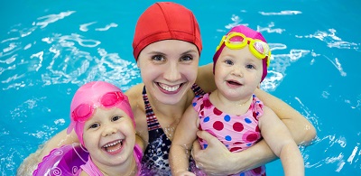 A mom is holding onto her two young children, who are using flotation devices, while in a swimming pool.