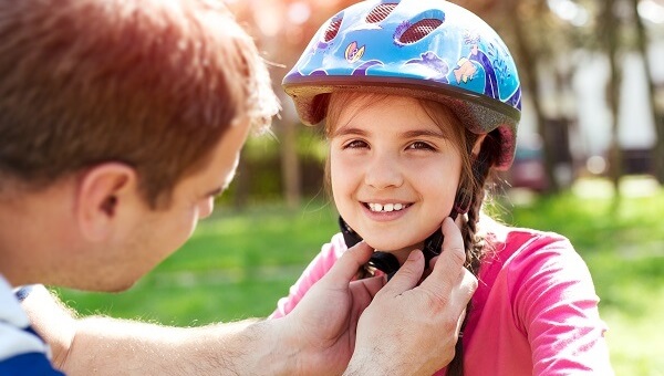 A father is adjusting the helmet on his little girl who is getting ready to ride her bicycle.