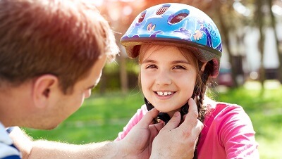 A father is adjusting the helmet on his little girl who is getting ready to ride her bicycle.