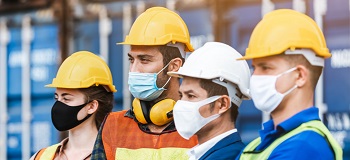 Four construction workers are wearing masks and helmets at their job site.