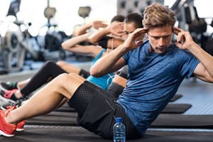 Muscular man doing sit ups at gym with other people in background.