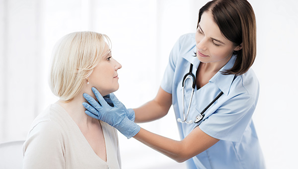 A female doctor is examining the neck of a female patient.